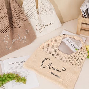 May include: Three knitted tote bags in beige, cream, and tan, each with a name in cursive script. The bags have a mesh design and are filled with items like a book and a bottle of juice. One bag says "Olivia Bridesmaid".