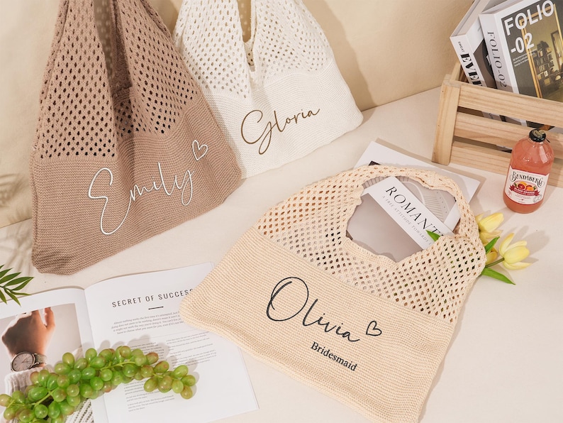 May include: Three knitted tote bags in beige, cream, and tan, each with a name in cursive script. The bags have a mesh design and are filled with items like a book and a bottle of juice. One bag says "Olivia Bridesmaid".