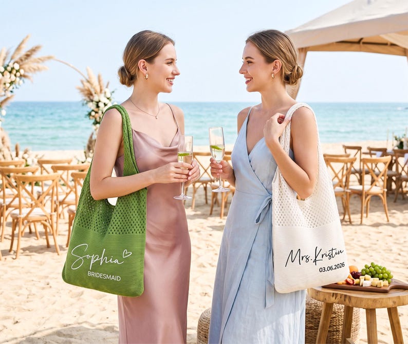 May include: Two women at a beach wedding, each holding a champagne flute. One carries a green tote bag with "Sophia Bridesmaid" printed on it. The other carries a white tote bag with "Mrs. Kristin 03.06.2026" printed on it. Both are wearing dresses.
