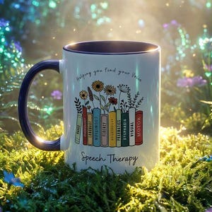 May include: White ceramic mug with a navy blue handle and rim, featuring the text "Helping you find your voice" and "Speech Therapy." The mug has a design of colourful books and flowers. The mug is set in a lush, green environment.