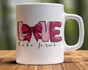 Op de afbeelding: Witte keramische mok met het woord "LOVE" in roze en rode letters, met een strik. De zin "like Jesus" staat onder het woord "LOVE" in cursief. De mok heeft een gebogen handvat.