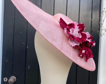 May include: A large, wide-brimmed hat made of pink straw with a burgundy and pink flower embellishment.