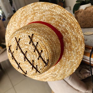May include: A straw hat with a red ribbon and brown stitching. The hat is made of woven straw and has a wide brim.