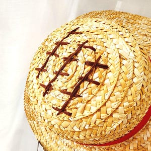 May include: A straw hat with a brown woven design and a red ribbon around the brim.