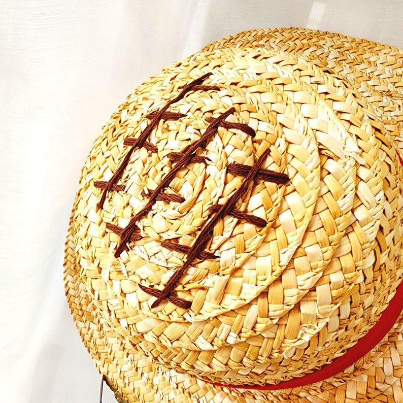 May include: A straw hat with a brown woven design and a red ribbon around the brim.