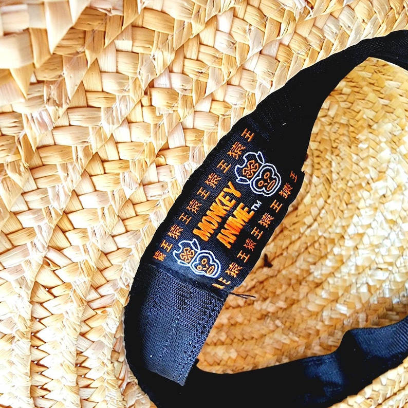 May include: A straw hat with a black band. The band has the text "MONKEY ANIME TM" in orange and black. The band also has a repeating pattern of a monkey face in black.
