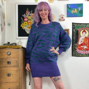 Könnte beinhalten: Ein lila Pulloverkleid mit grünem Zickzackmuster. Das Kleid hat lange Ärmel und einen gerippten Saum. Die Frau auf dem Bild trägt das Kleid.