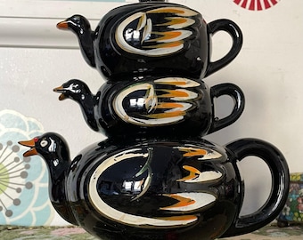 Juego de té vintage de loza roja con patos apilados; tetera esmaltada en negro, crema y azucarero.
