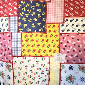 May include: A patchwork quilt featuring floral and geometric designs in red, yellow, blue, pink, and white. The quilt measures 183 x 229 cm. It has a red rope-like border around the edges.