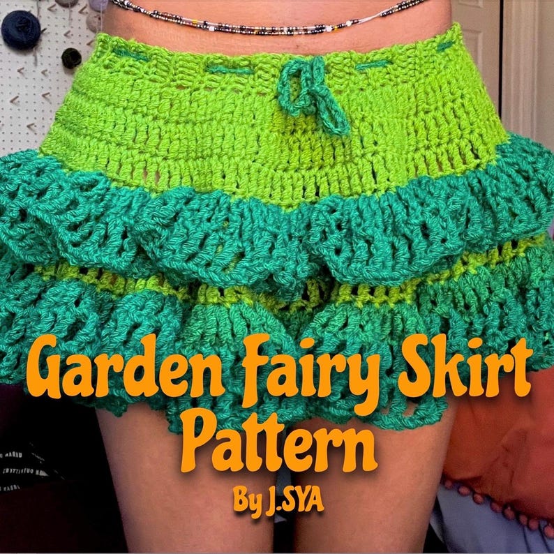 K&ouml;nnte beinhalten: Ein gr&uuml;ner H&auml;kelrock mit mehreren R&uuml;schenlagen. Der Rock ist mit einem gr&uuml;nen Band in der Taille gebunden. Der Text "Garden Fairy Skirt Pattern By J.SYA" ist auf den Rock gedruckt.