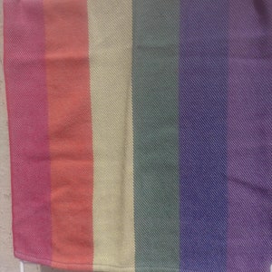 Two folded handwoven rainbow pride hand towels hang side by side, one showing red, orange, and yellow stripes, the other green, blue, and purple stripes. Each stripe is just shy of 3 inches wide.