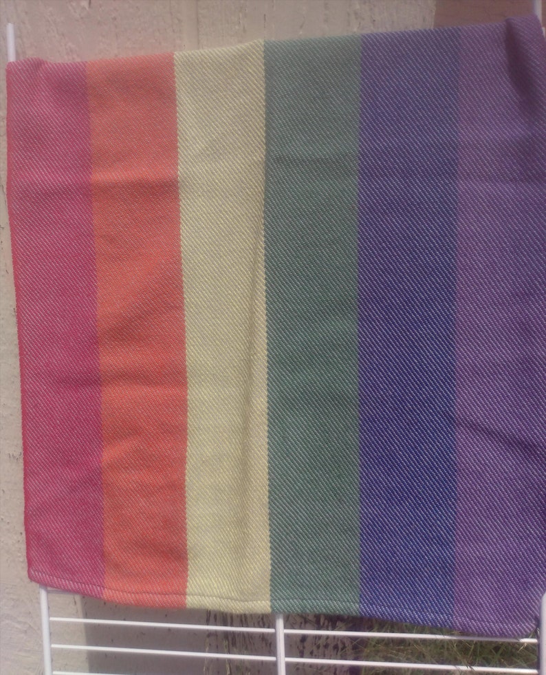 Two folded handwoven rainbow pride hand towels hang side by side, one showing red, orange, and yellow stripes, the other green, blue, and purple stripes. Each stripe is just shy of 3 inches wide.