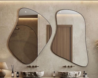 Puede incluir: Un baño moderno con dos lavabos y un tocador flotante. Los lavabos están hechos de piedra gris clara y tienen una forma orgánica única. El tocador está hecho de madera y tiene dos cajones. El baño tiene un suelo de ajedrez negro y blanco y dos grandes espejos de forma orgánica con marcos negros.
