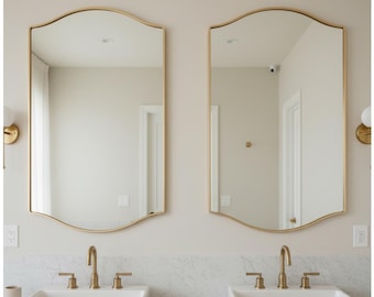 May include: Two rectangular mirrors with gold frames and a scalloped top are mounted above two white sinks with gold taps. The sinks are set on a marble countertop. The bathroom has a neutral colour palette.