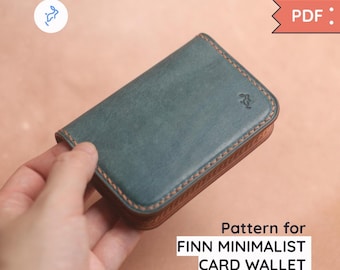 May include: A teal card wallet with brown stitching and a brown border. The wallet has a minimalist design and the text "Pattern for FINN MINIMALIST CARD WALLET". A small logo is visible on the top left.