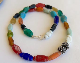 May include: A colorful necklace made of various glass beads in shades of red, orange, yellow, green, blue, and white. The necklace features a silver clasp and a silver bead with a textured design.