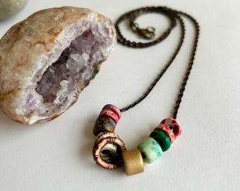 May include: A necklace with a bronze chain and colorful ceramic beads. The beads are pink, green, and brown with white accents.