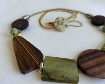 May include: A wooden and green stone necklace with a variety of shapes and sizes. The necklace is strung on a brown cord and has a small, round, speckled stone button.