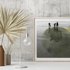 K&ouml;nnte beinhalten: Ein gerahmtes Schwarzwei&szlig;foto von Menschen, die an einem Strand entlanglaufen, mit einem gr&uuml;nen und gelben Aquarelleffekt. Das Foto ist in einem hellen Holzrahmen gerahmt.