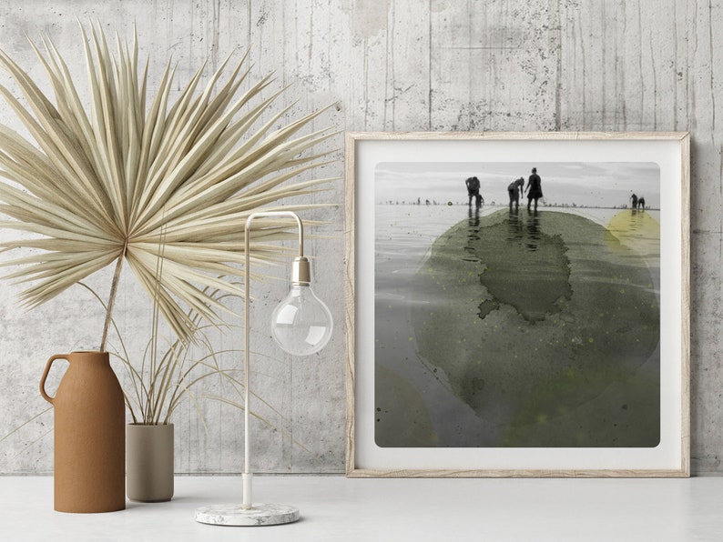 K&ouml;nnte beinhalten: Ein gerahmtes Schwarzwei&szlig;foto von Menschen, die an einem Strand entlanglaufen, mit einem gr&uuml;nen und gelben Aquarelleffekt. Das Foto ist in einem hellen Holzrahmen gerahmt.