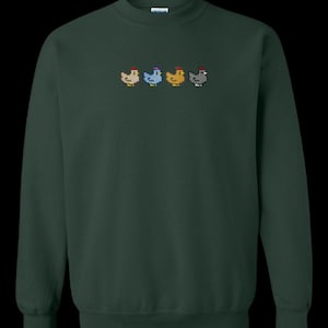 K&ouml;nnte beinhalten: Ein dunkelgr&uuml;ner Pullover mit einem Pixel-Design aus f&uuml;nf H&uuml;hnern in einer Reihe. Die H&uuml;hner sind in verschiedenen Farben: wei&szlig;, blau, gelb, braun und grau.