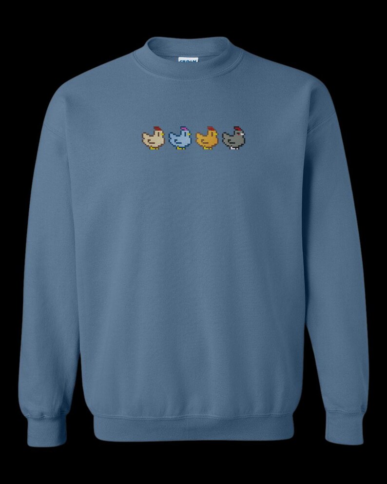 K&ouml;nnte beinhalten: Ein blaues Sweatshirt mit einer Reihe von f&uuml;nf gestickten, pixelartigen H&uuml;hnern in verschiedenen Farben.