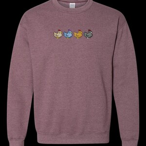 K&ouml;nnte beinhalten: Ein heidefarbenes Sweatshirt mit einem pixeligen Design von vier H&uuml;hnern in einer Reihe. Die H&uuml;hner sind in verschiedenen Farben: rot, blau, gelb und grau.