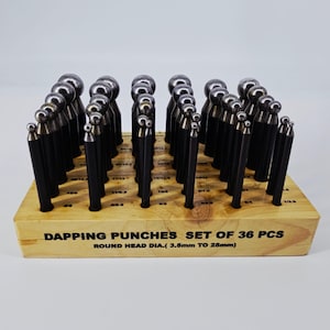 May include: A set of 36 dapping punches with round heads, displayed in a wooden block. The punches have black handles and silver heads, with sizes ranging from 3.5mm to 25mm. The text "DAPPING PUNCHES SET OF 36 PCS" is visible on the block.