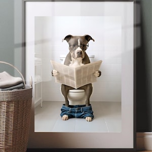 May include: Framed print featuring a dog wearing glasses and reading a newspaper while sitting on a toilet. The dog is wearing blue jeans. The bathroom has white tile and a wicker basket.