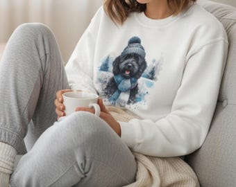 Könnte beinhalten: Weißes Sweatshirt mit einer Aquarellillustration eines schwarzen Hundes, der eine blaue Mütze und einen Schal in einer Schneelandschaft trägt. Der Hund lächelt. Das Sweatshirt ist ein lässiger, bequemer Stil.
