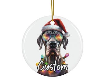 Peut inclure: Ornement de Noël rond et blanc représentant un Grand Danois portant un bonnet de Père Noël et des lunettes de soleil arc-en-ciel. Le chien est orné d'une guirlande lumineuse colorée et le mot "Custom" est écrit en dessous.