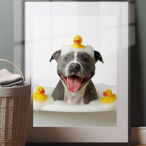 May include: A framed print featuring a gray and white dog in a bubble bath with yellow rubber duckies. The dog has a rubber ducky on its head and is smiling with its tongue out. A wicker basket is in the foreground.