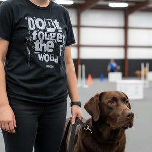 May include: A black t-shirt with the text "Don't forget the wood" in white, with the hashtag #FINISH. A brown Labrador Retriever is on a leash next to the person wearing the shirt.