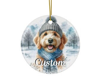 May include: Round ceramic ornament featuring a watercolor illustration of a golden doodle dog wearing a gray knit hat and blue scarf. The word "Custom" is printed in script. A gold string is attached for hanging. Winter scene background.