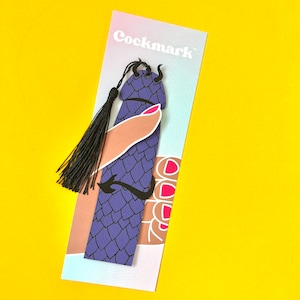 May include: Purple bookmark with a dragon design and a black tassel. The bookmark is held by a hand with pink nail polish. The bookmark has the text "Cockmark" printed on it.