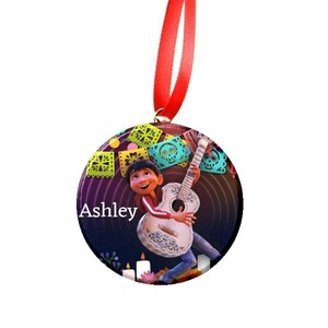 May include: Round Christmas ornament featuring a cartoon character playing a guitar. The character is surrounded by colorful paper decorations. The ornament is personalized with the name "Ashley".