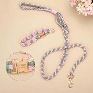 May include: A dog leash and collar set in pink, green, and white, with a braided design. The leash includes a handle and a gold-coloured clasp. The collar has small pink flower details and a gold-coloured buckle with the word "Custom" and a phone number.