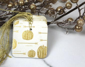 May include: A stack of white gift tags with a gold pumpkin and arrow pattern. The tags have a gold string attached.