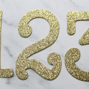 May include: Gold glitter numbers 1, 2, and 3. The numbers are cut out of cardstock and have a sparkly finish.