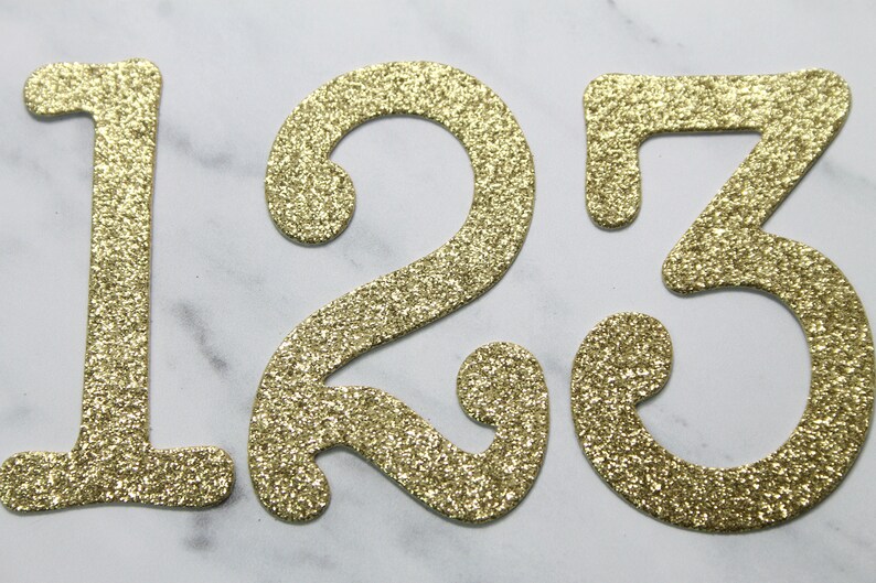 May include: Gold glitter numbers 1, 2, and 3. The numbers are cut out of cardstock and have a sparkly finish.