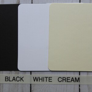 K&ouml;nnte beinhalten: Drei quadratische Muster aus Karton in Schwarz, Wei&szlig; und Creme. Der Text "BLACK", "WHITE" und "CREAM" ist unter den Mustern gedruckt.
