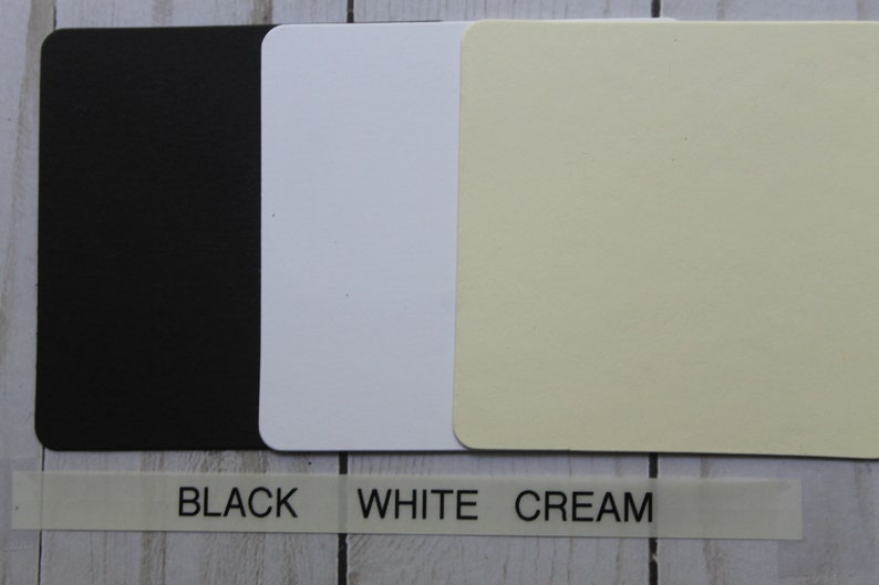 K&ouml;nnte beinhalten: Drei quadratische Muster aus Karton in Schwarz, Wei&szlig; und Creme. Der Text "BLACK", "WHITE" und "CREAM" ist unter den Mustern gedruckt.