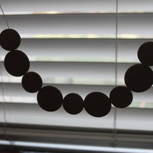 May include: A black beaded garland hangs in front of a white window blind. The beads are round and evenly spaced.