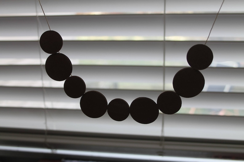 May include: A black beaded garland hangs in front of a white window blind. The beads are round and evenly spaced.