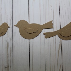 May include: Three brown paper bird cutouts on a white wood background. The birds are different sizes and shapes.