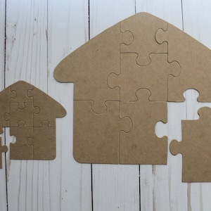 May include: Two brown wooden house-shaped jigsaw puzzles, one larger than the other, with a piece missing from each. The puzzles are on a white wooden background.