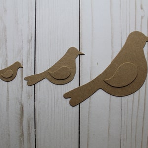 May include: Three brown paper bird cutouts of varying sizes. The birds are arranged in a row from smallest to largest, with the largest bird on the right.