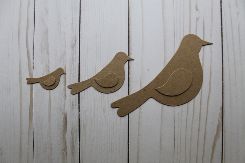 May include: Three brown paper bird cutouts of varying sizes. The birds are arranged in a row from smallest to largest, with the largest bird on the right.