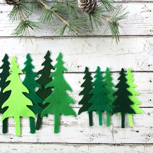 May include: A set of eight felt Christmas trees in various shades of green, arranged in a row on a white wooden background.