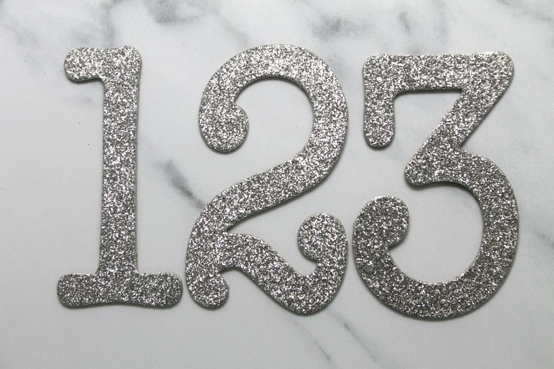 May include: Silver glitter numbers 1, 2, and 3 on a white marble background.